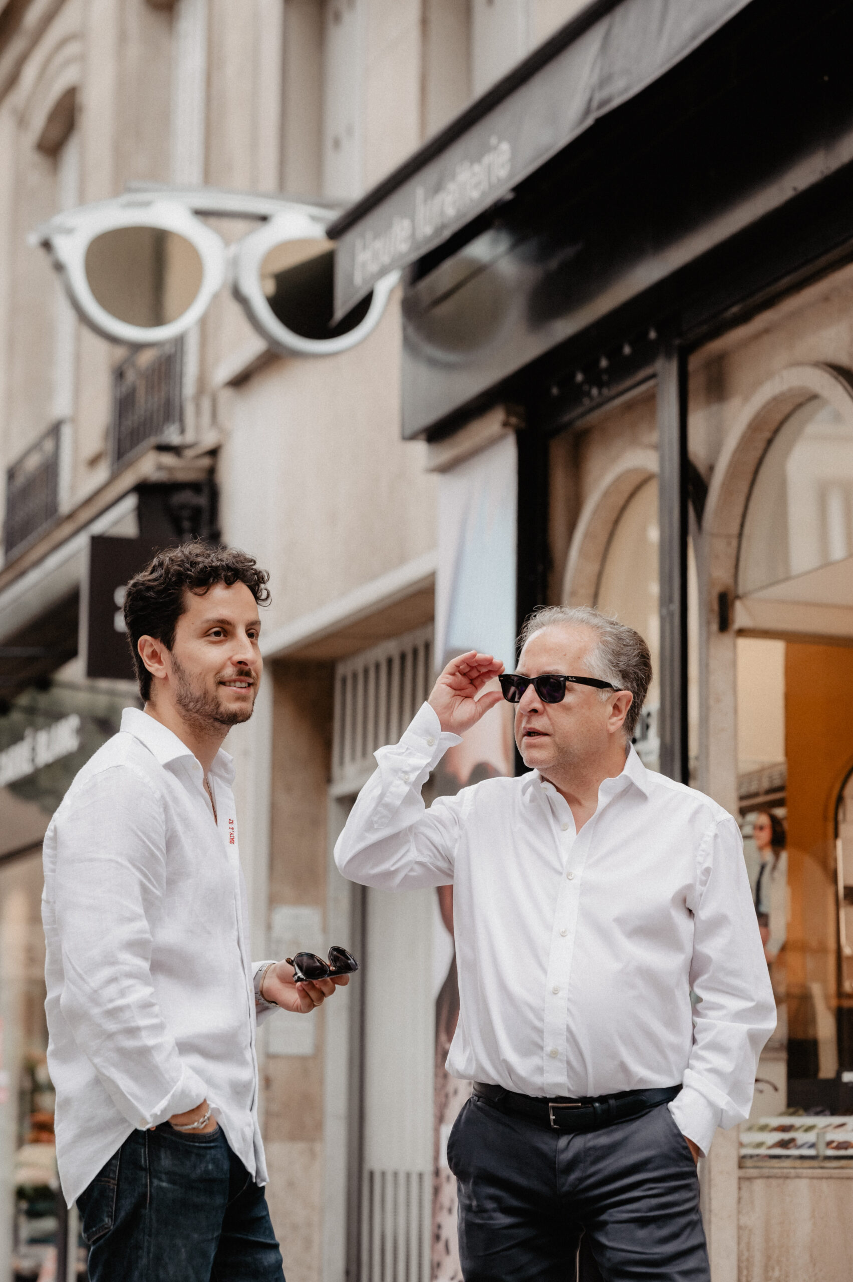 Pere et Fils Gualdoni, Opticien Paris 16 devant la boutique ajustant ses lunettes de soleil devant sa boutique
